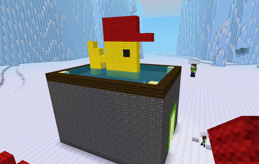 A blocky sculpture of a stone house with a big yellow fish wearing a red hat on the roof.